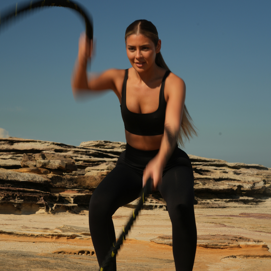 Woman exercising with battle ropes outdoors on rocky terrain.