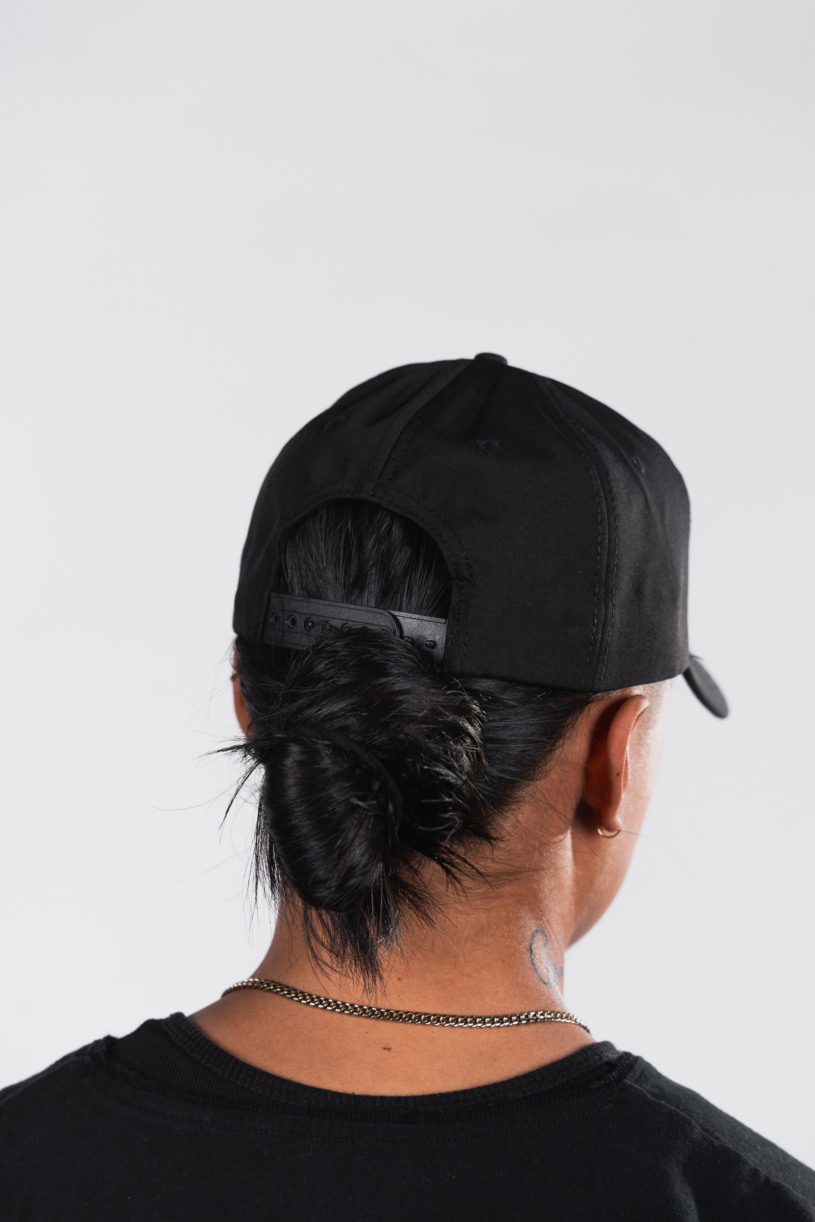 Person with black cap and bun, viewed from behind.