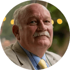 A circular headshot of an older man with a mustache, wearing a suit jacket and tie.
