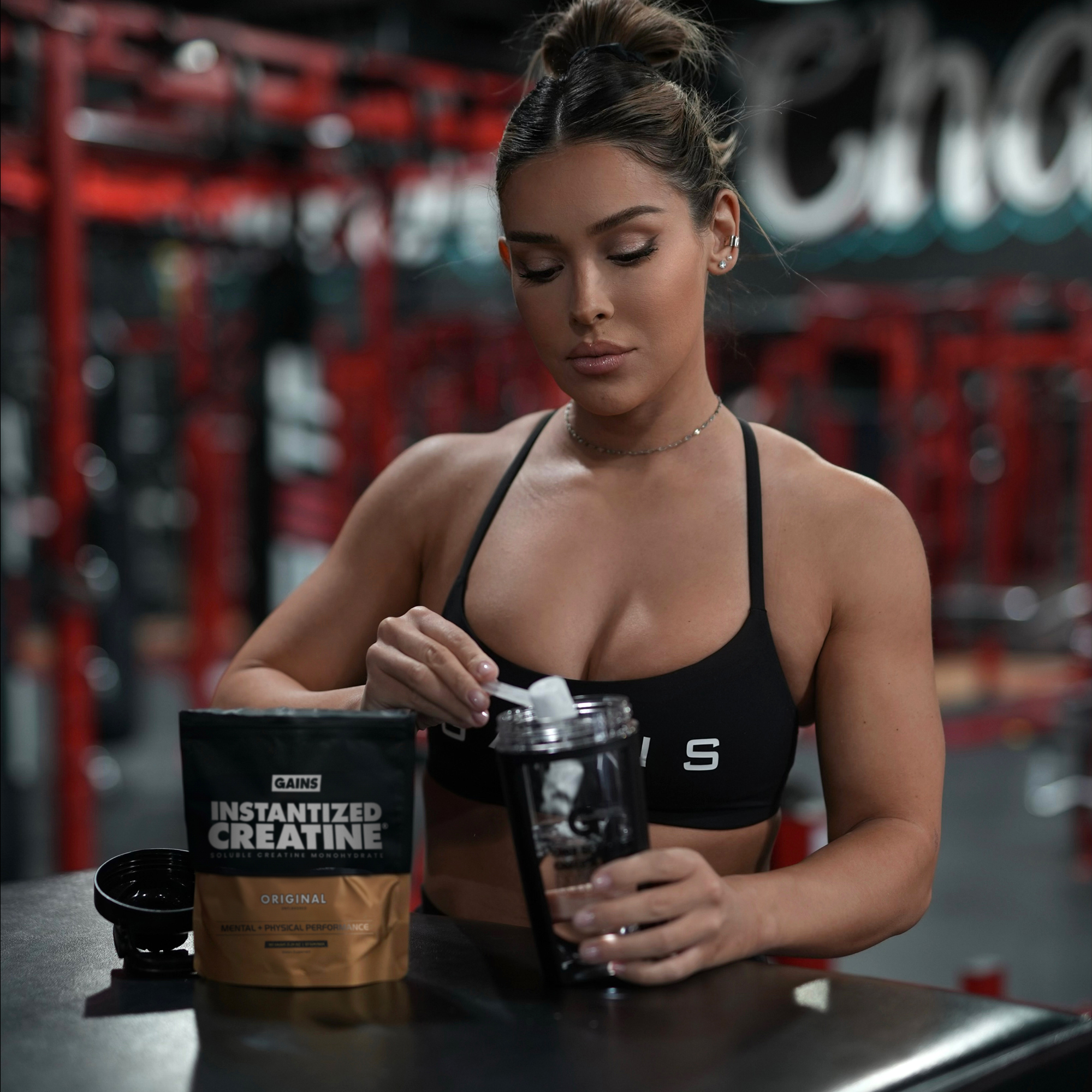 Woman preparing a creatine supplement in a gym setting.