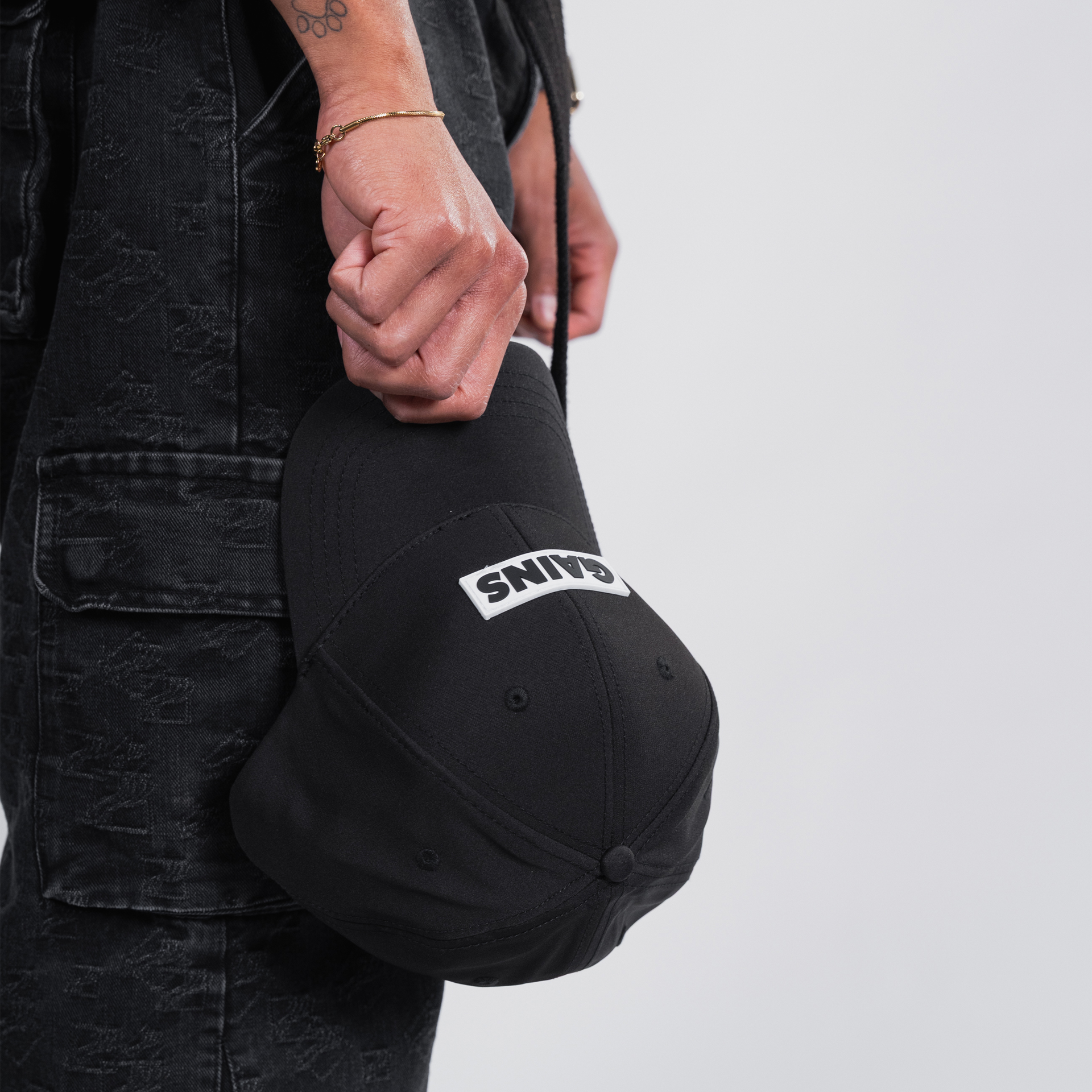 Person holding a black cap with 'GAINS' text, wearing dark clothing.