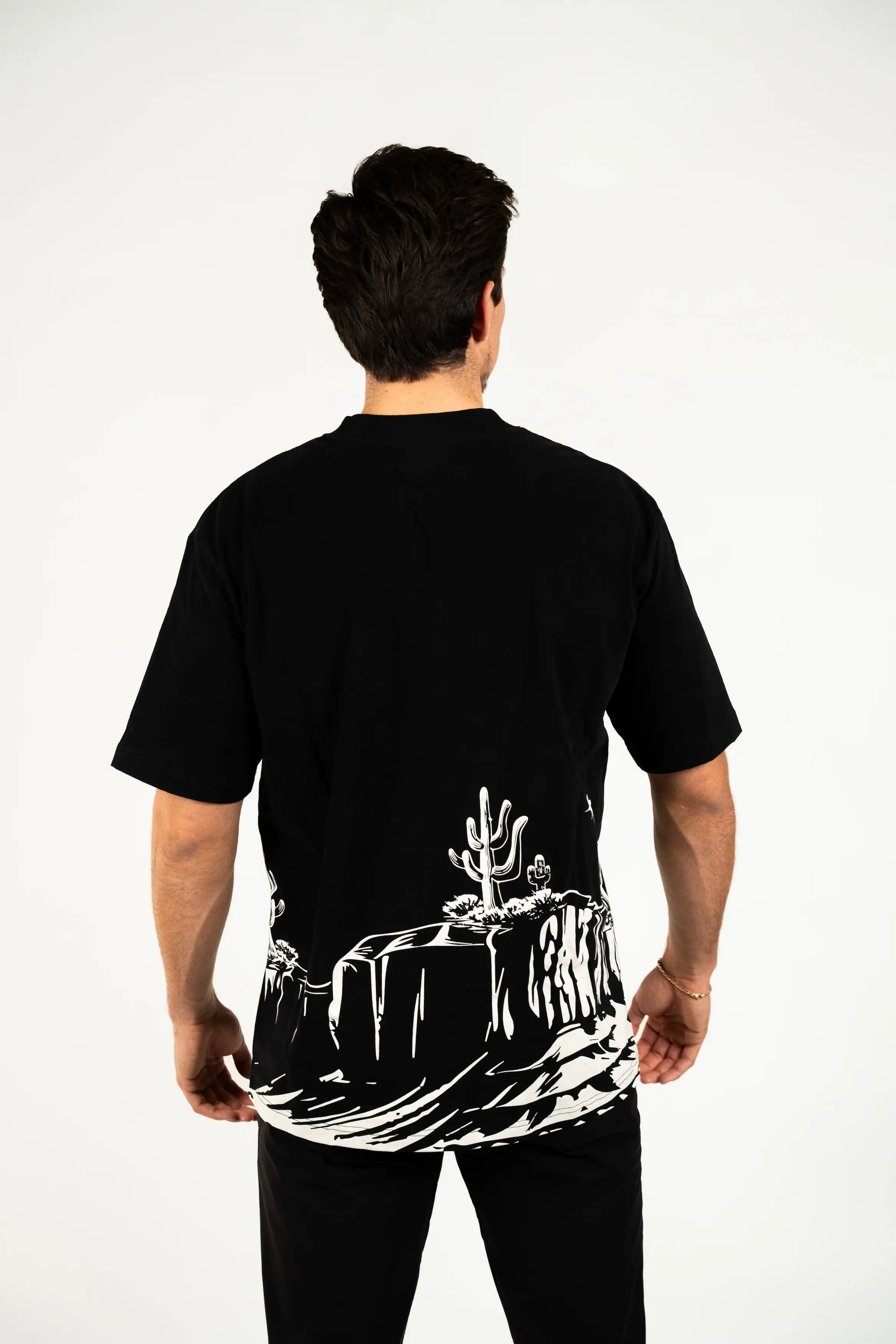 Person wearing a black t-shirt with a desert landscape design on the back.