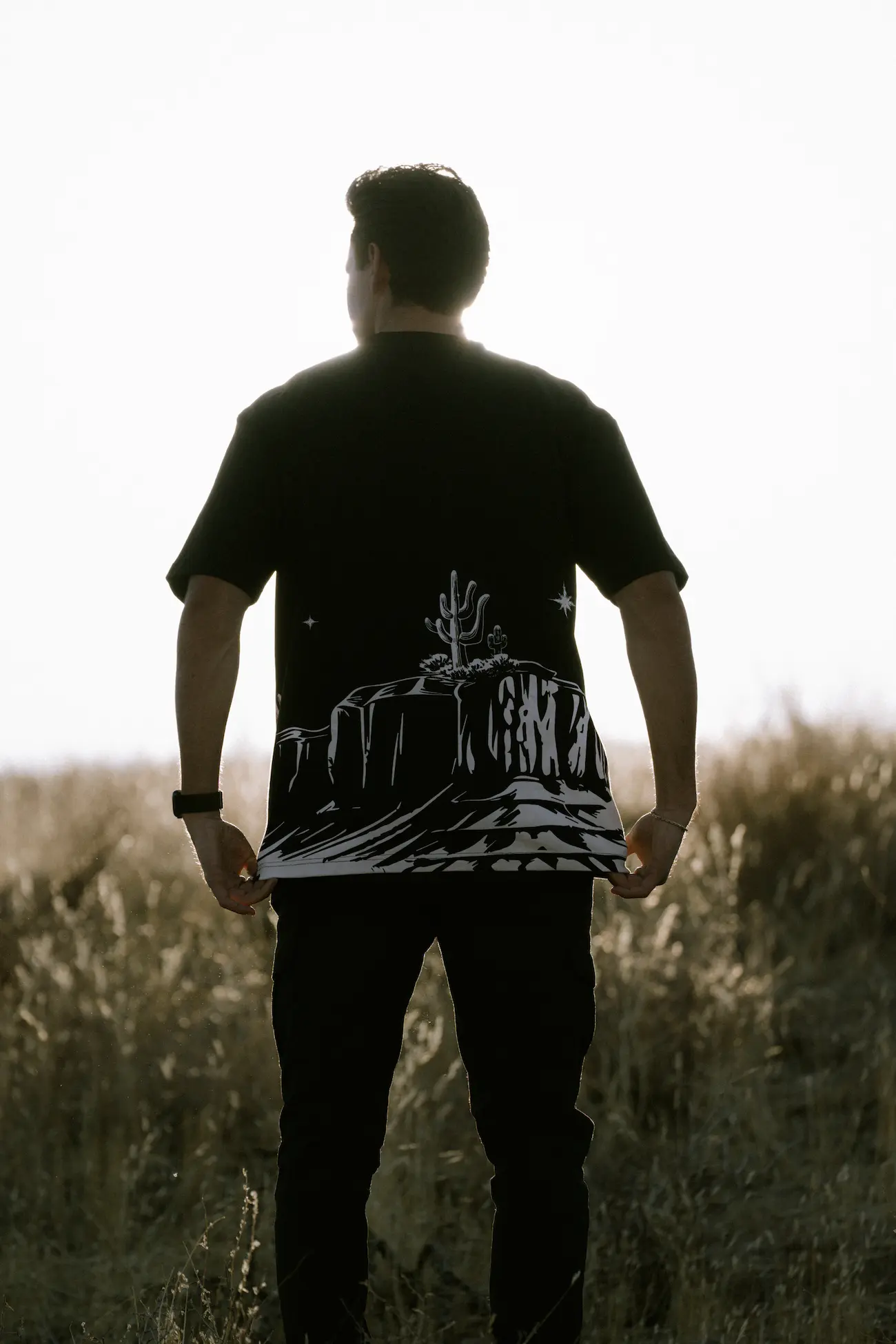 Man in a field, wearing a desert-themed T-shirt.