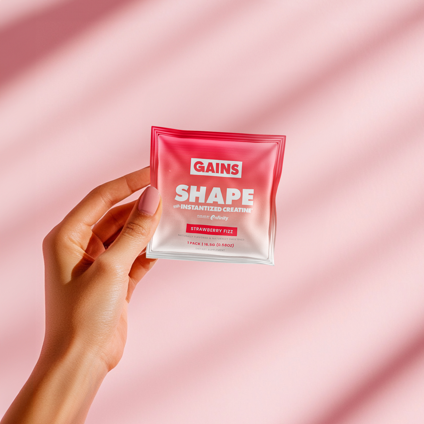 Hand holding a pink packet labeled 'GAINS SHAPE' on a pink background.