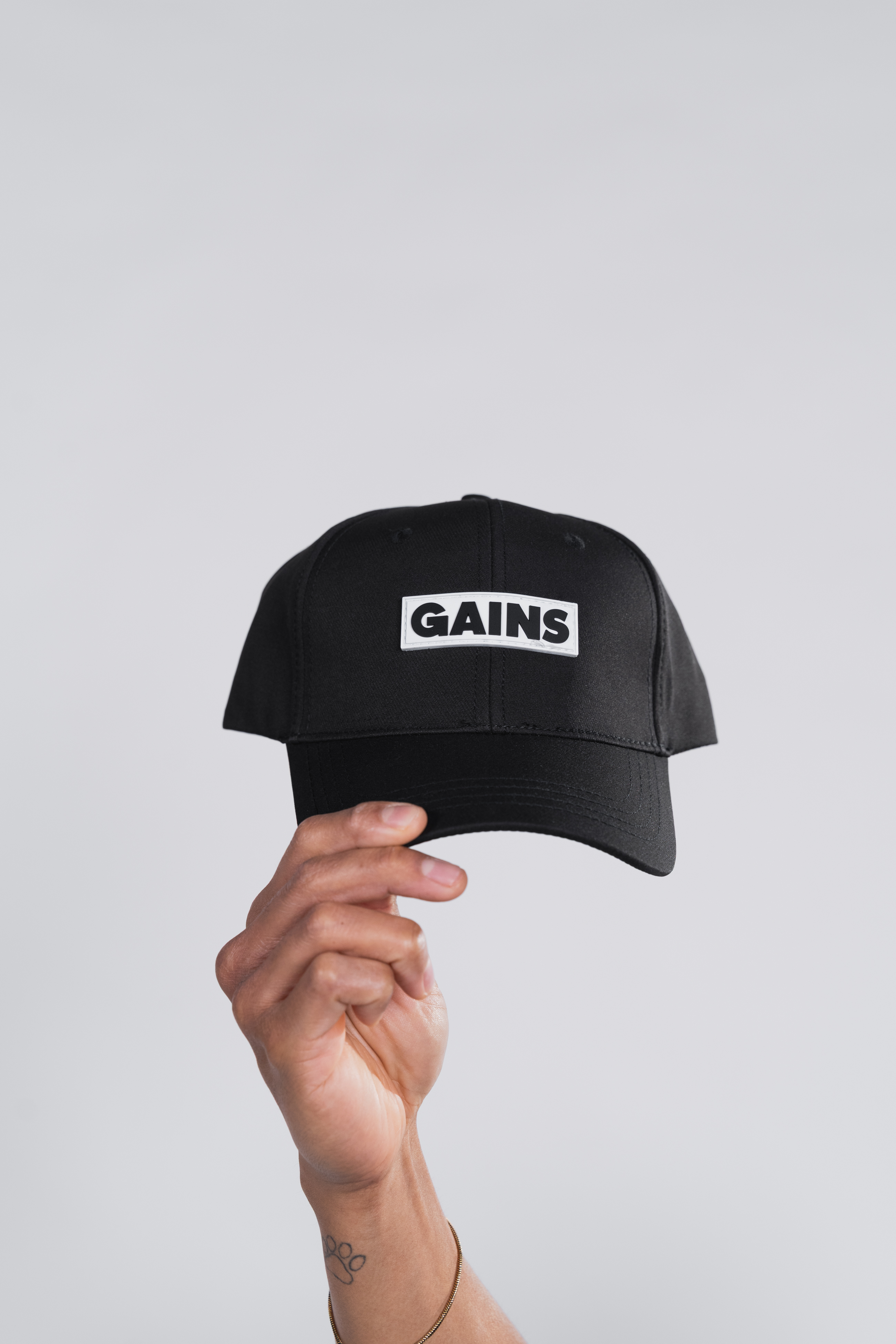 Hand holding a black cap with 'GAINS' text on it.