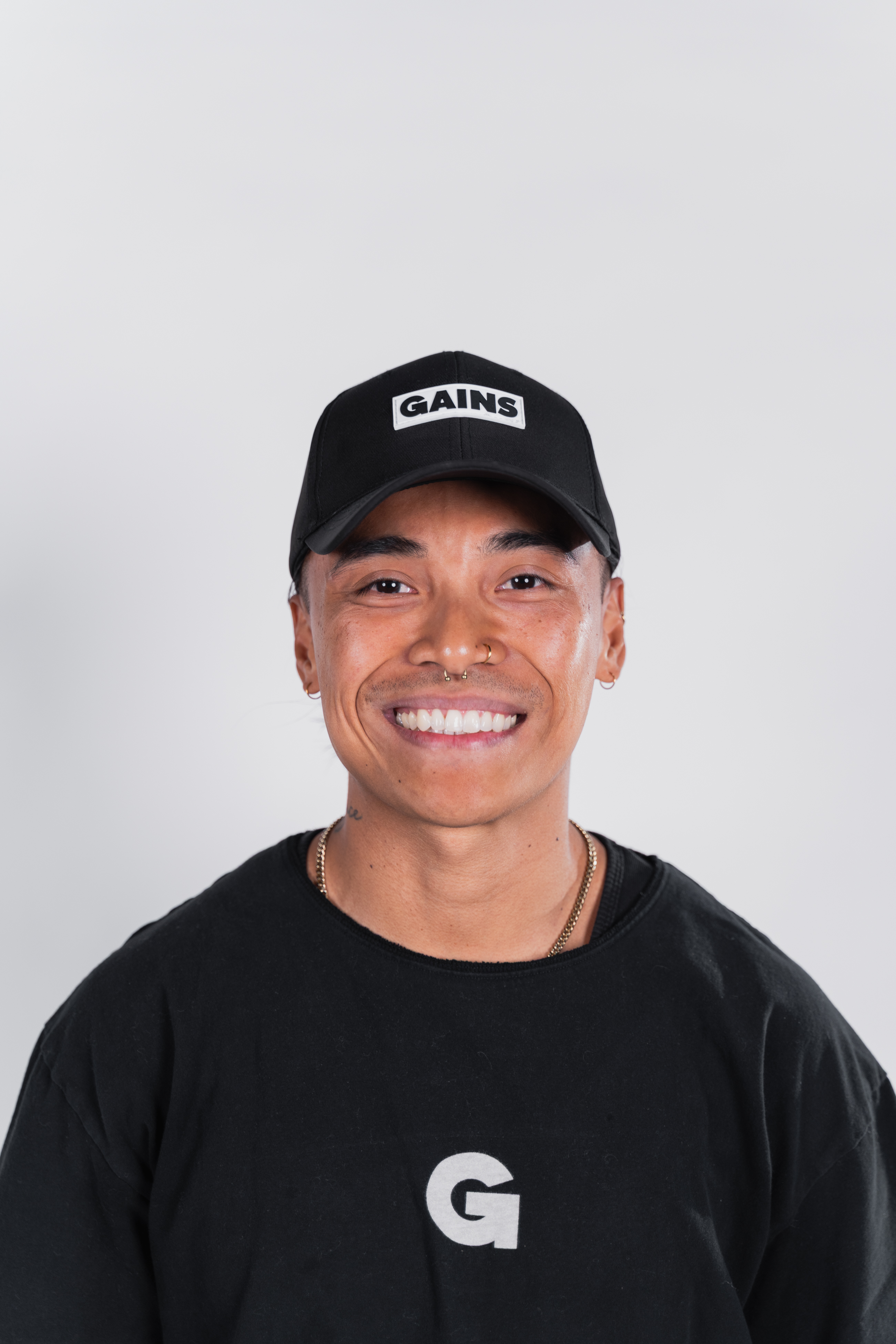 Person smiling, wearing a black cap with 'GAINS' and a black shirt with 'G'.