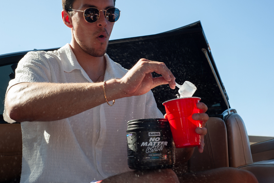 Man in sunglasses mixing powder into a red cup outdoors.