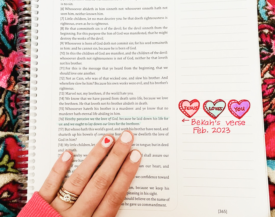 Hand on open book with handwritten note 'Jesus loves you' and decorated hearts.