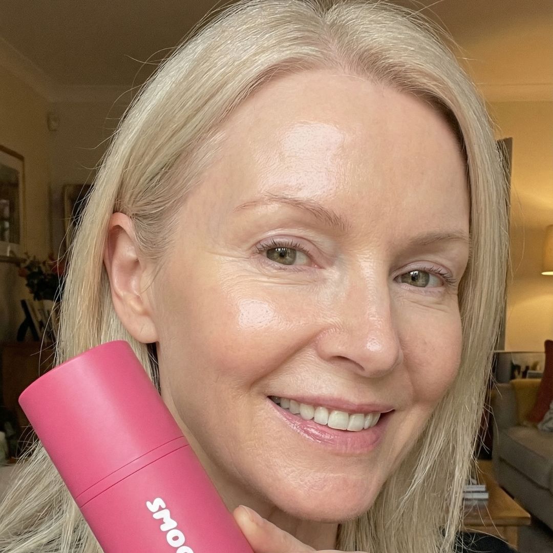 Person smiling, holding a pink container indoors.