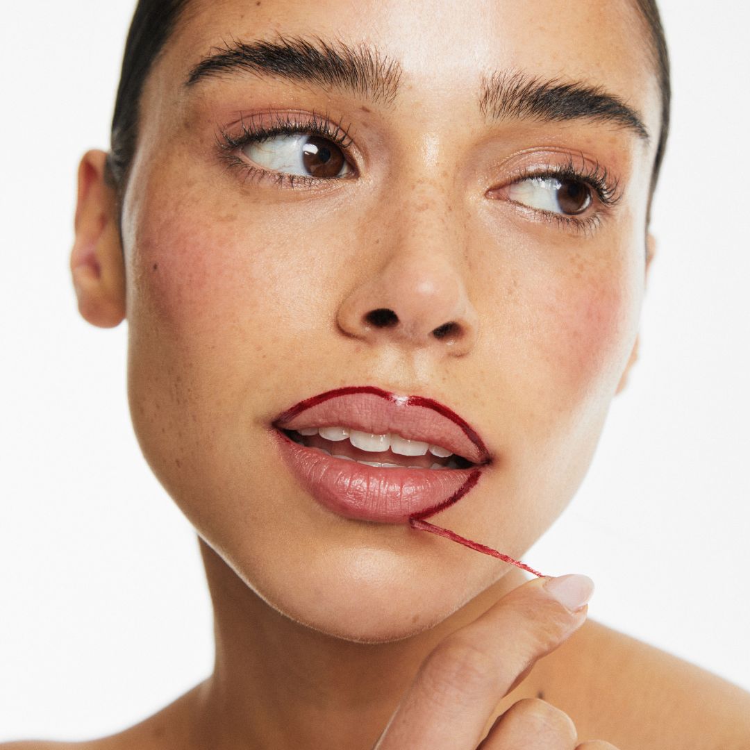 Person with red lipstick outline, pulling a thread from lips.