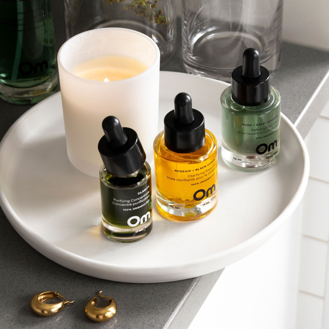 Three dropper bottles and a lit candle on a white tray.