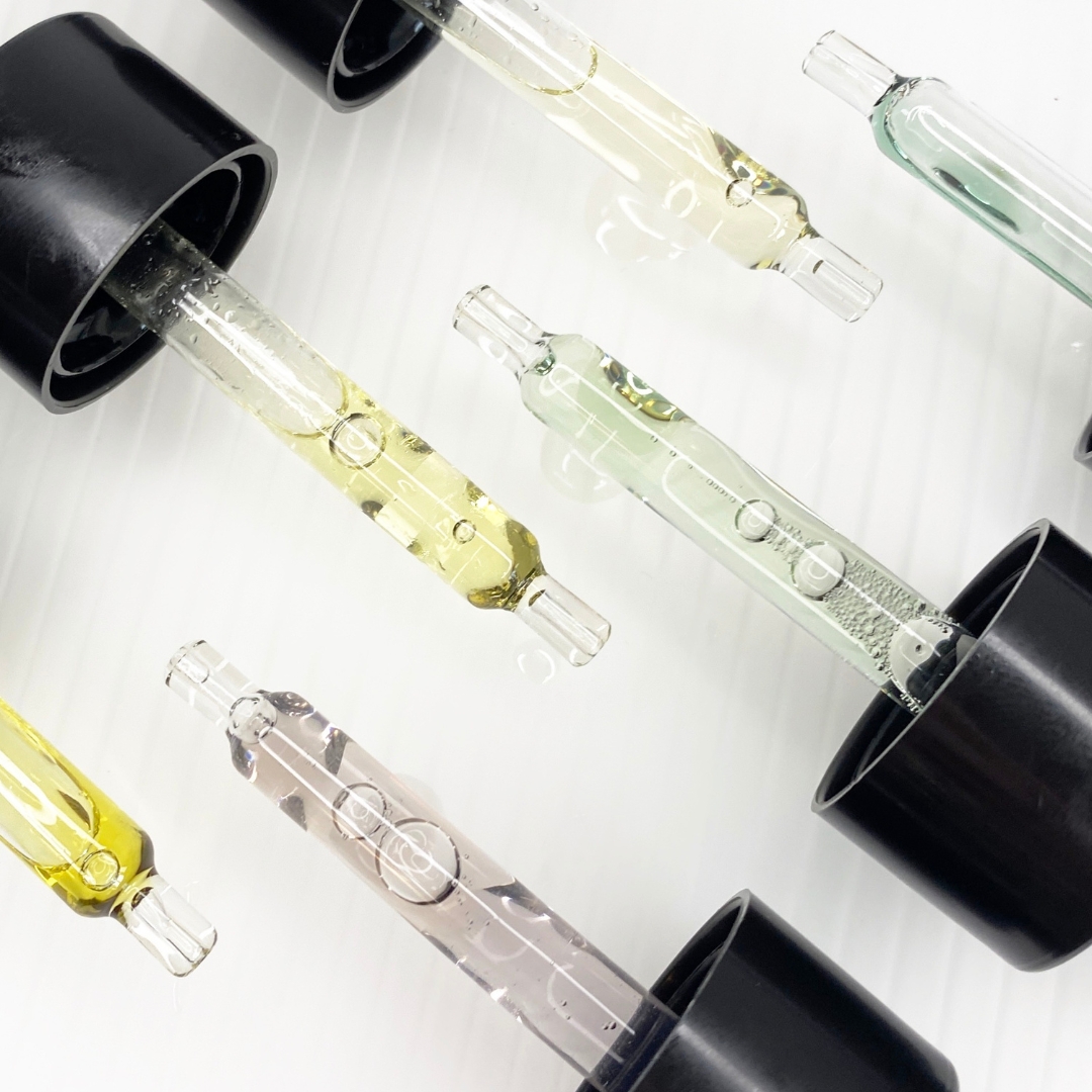 Close-up of glass droppers with colored liquids and black caps.