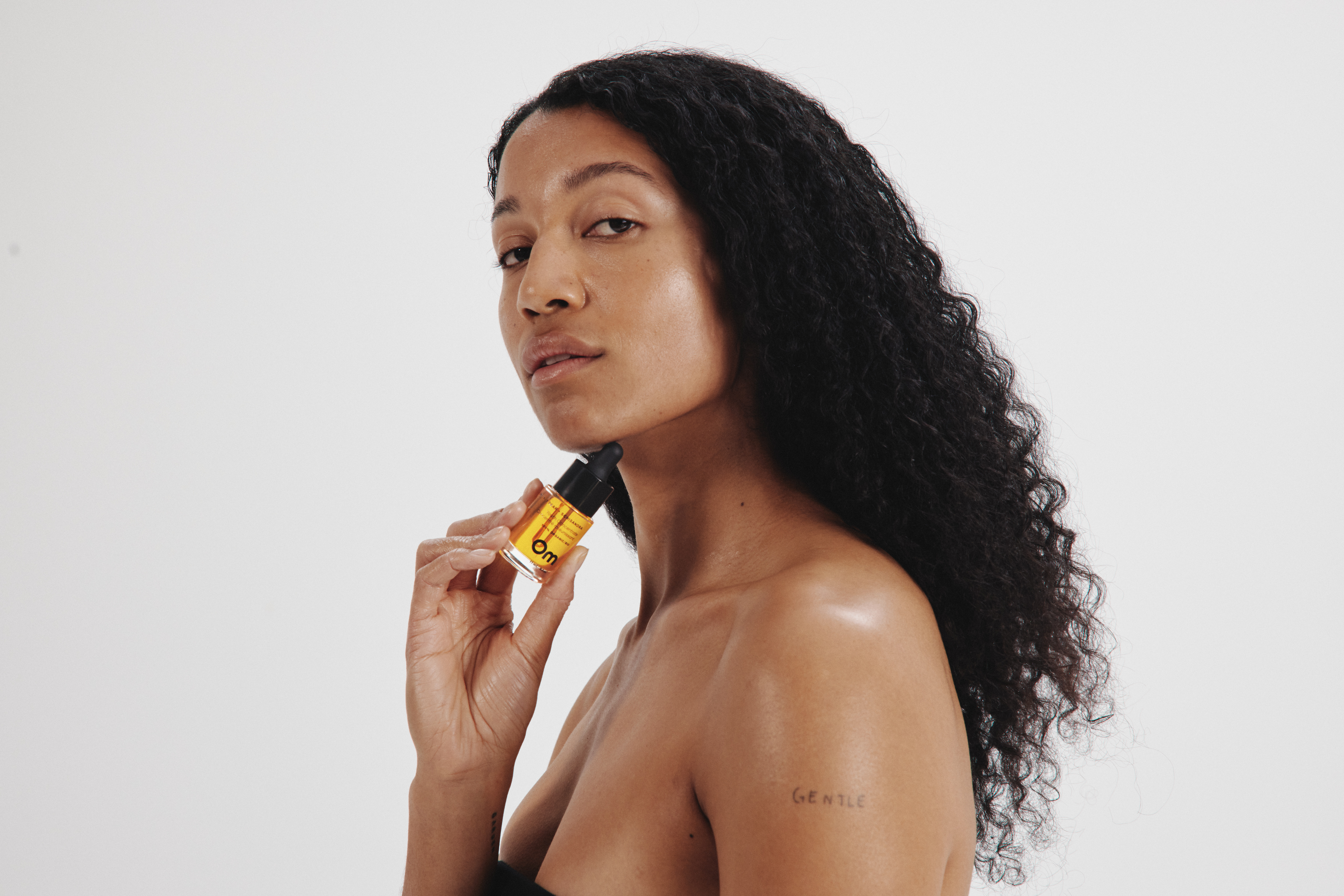 Person holding a small bottle of yellow liquid against their chin.