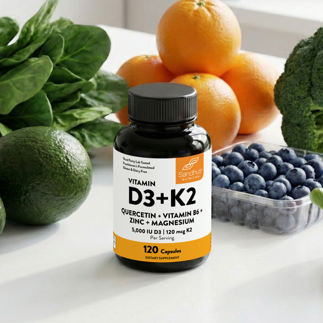A bottle of Sandhus Nutrition Vitamin D3+K2 supplements sits amongst fresh fruits and vegetables.