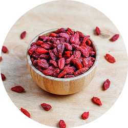 A small wooden bowl filled with dried red goji berries on a wooden surface.