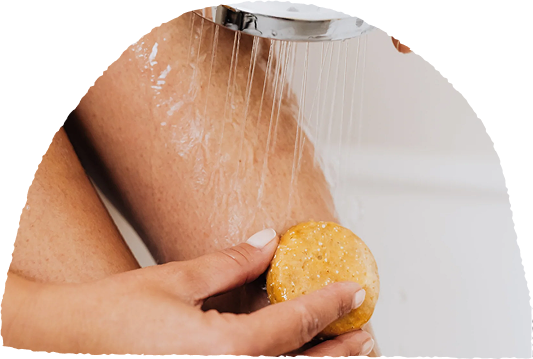 Person holding a round soap under a shower stream.