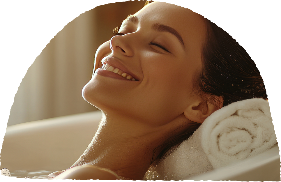A person smiling and relaxing in a bath with a towel pillow.