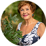 Smiling person in floral dress standing outdoors near green leaves.