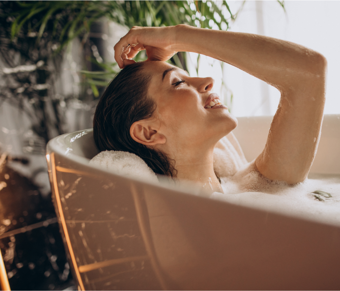 Woman enjoying a relaxing bath with bubbles, smiling in a well-lit bathroom.