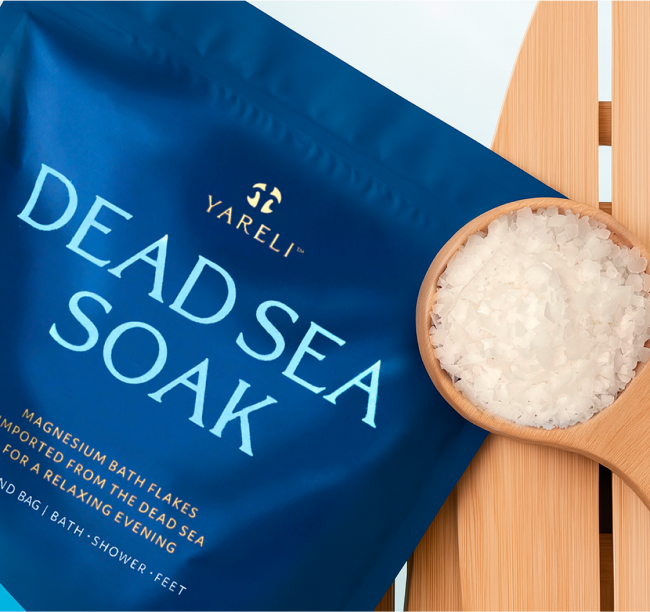 Blue bag labeled 'Dead Sea Soak' with scoop of bath flakes on wood surface.