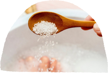 Wooden spoon pouring bath salts into a relaxing bath.