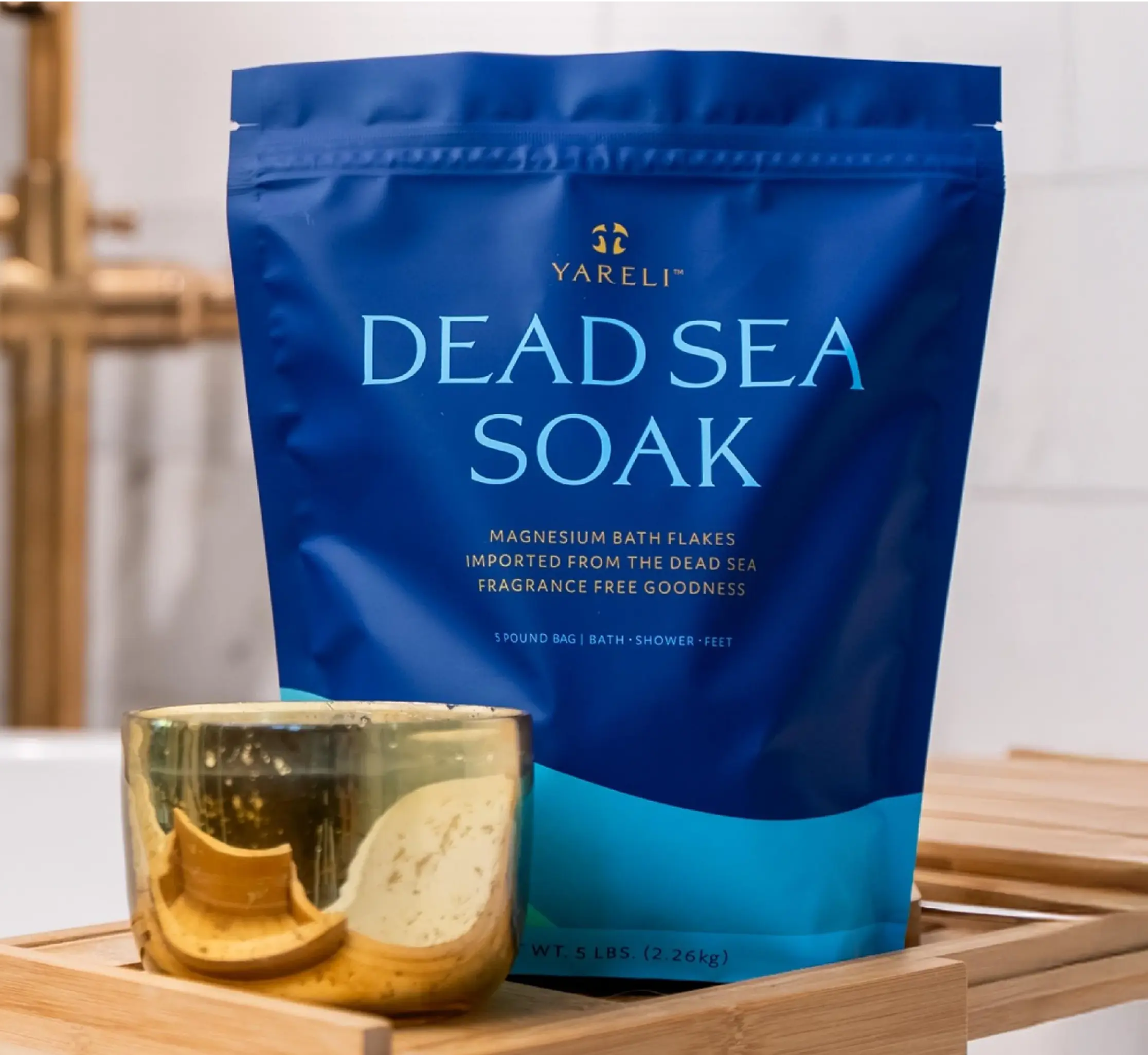 Blue bag of Dead Sea Soak with a gold cup on a wooden tray.