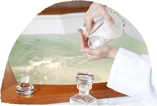 Person in bathrobe pouring bath salts into a bathtub.