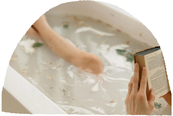 Person reading a book in a bathtub filled with milky water and green leaves.