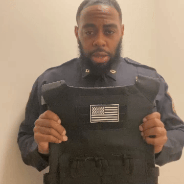 Person in a uniform holding a black vest with an American flag patch.