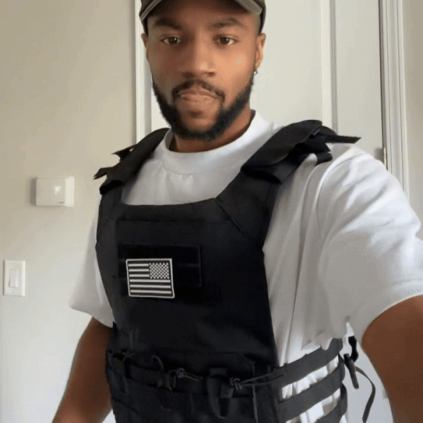 Person wearing a black tactical vest with a flag emblem, standing indoors.