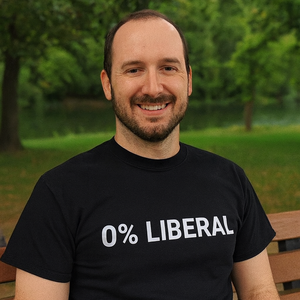 A person sitting on a bench outdoors, wearing a t-shirt with text.