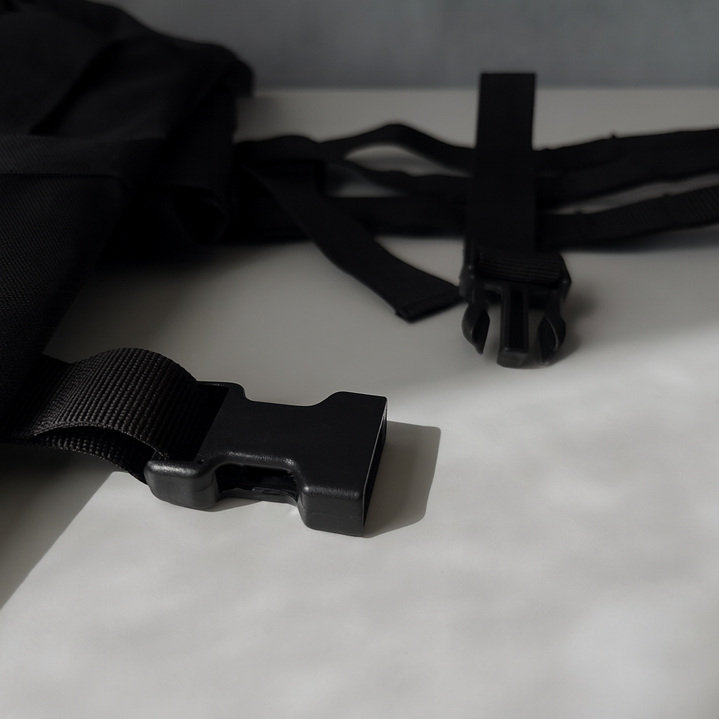 Close-up of black backpack straps and buckle on a light surface.