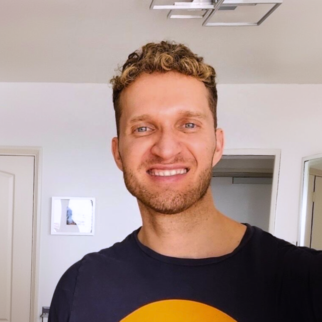 Person smiling in a room with white walls and a door.