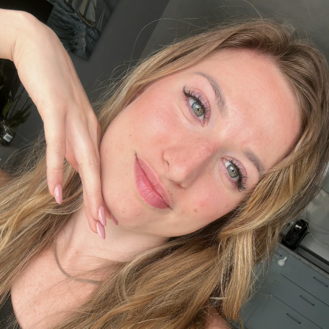 Person with long hair posing indoors, hand under chin.