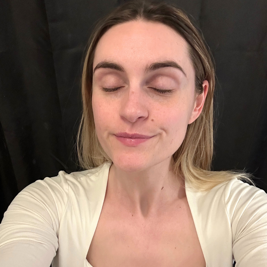 Person with closed eyes, wearing a white top, against a dark background.