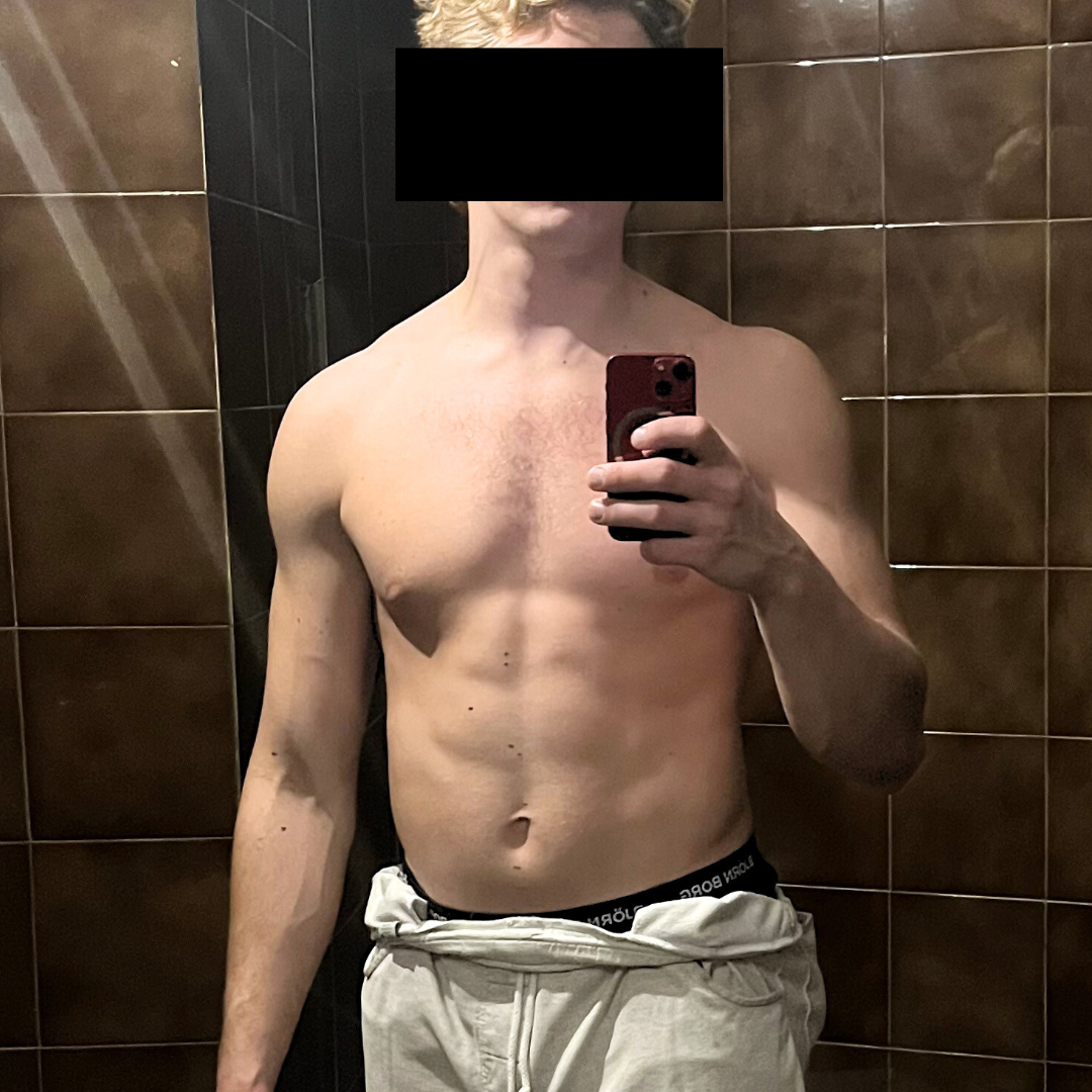 Shirtless person taking a mirror selfie in a tiled room.