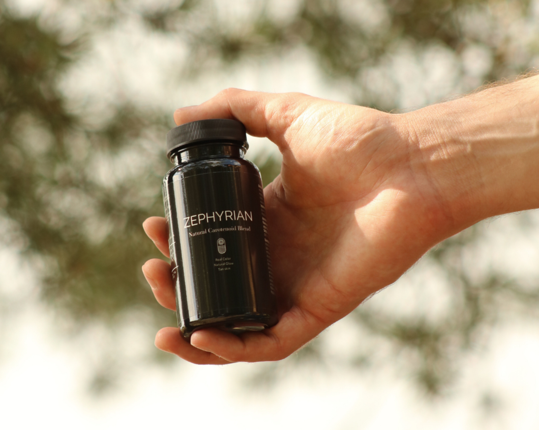 Hand holding a black bottle labeled 'Zephyrian' against a blurred background.