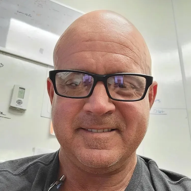 Bald man with glasses smiling in an office setting.