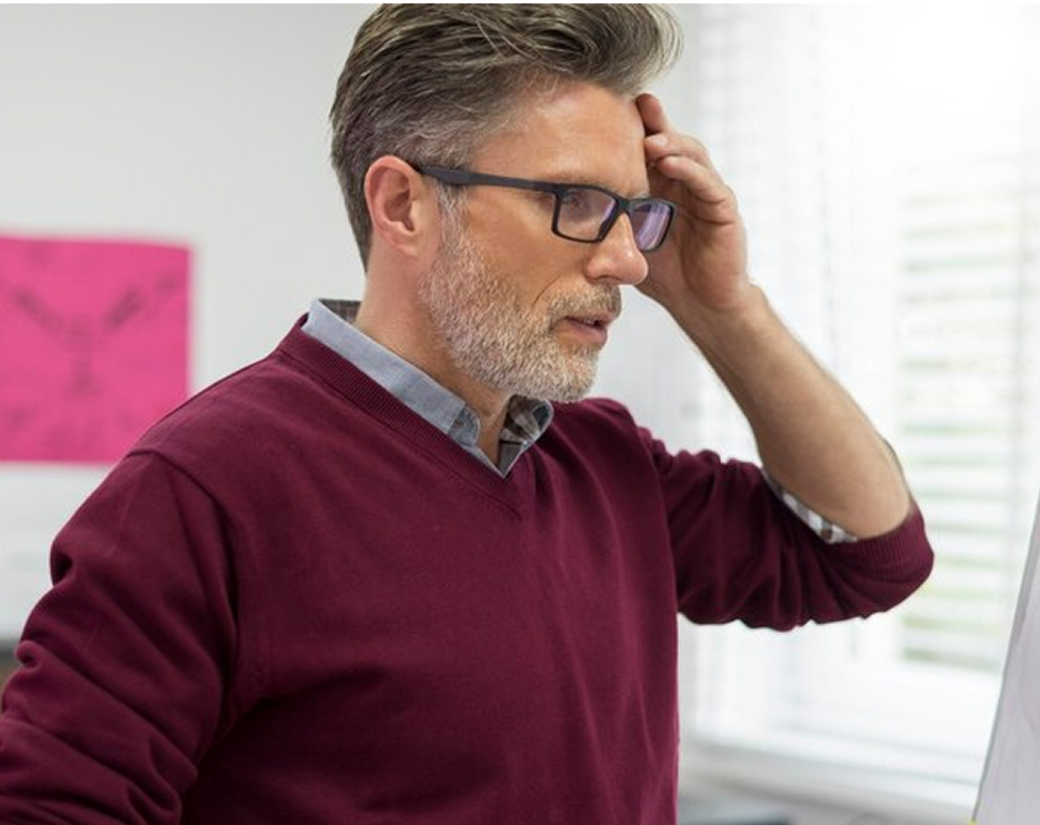 Man with glasses and beard looking at a whiteboard, appearing thoughtful.