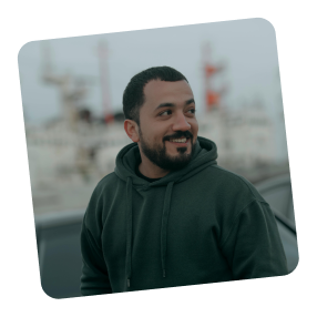 Person smiling, wearing a dark hoodie, with a blurred outdoor background.