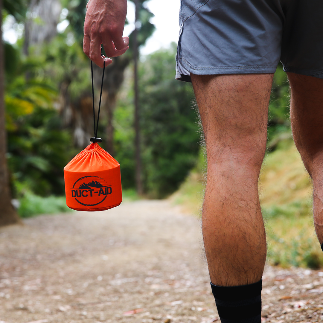 Person holding an orange bag labeled 'DUCT-AID' on a forest path.