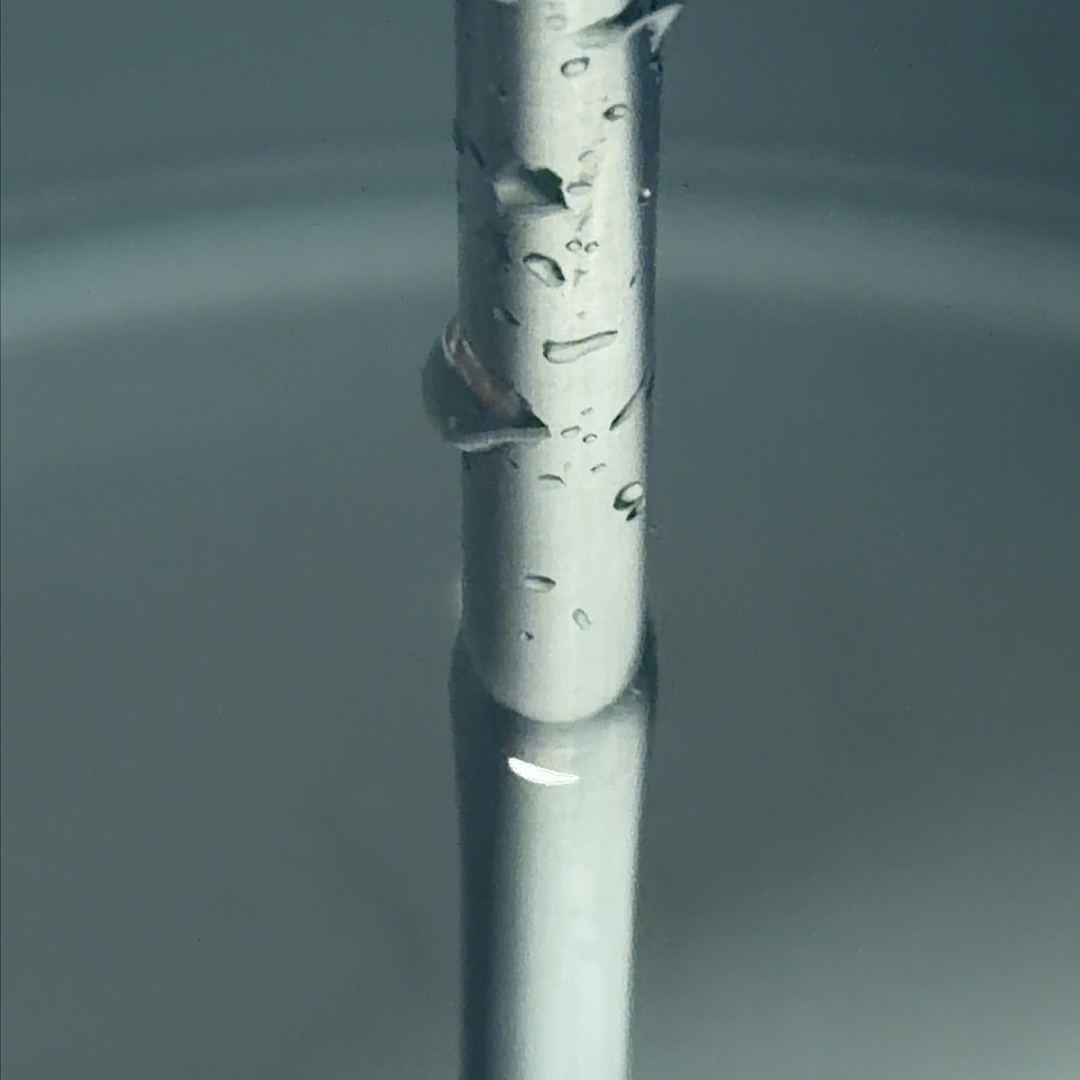 A close-up of a metal rod with water droplets on its surface, partially submerged in liquid.