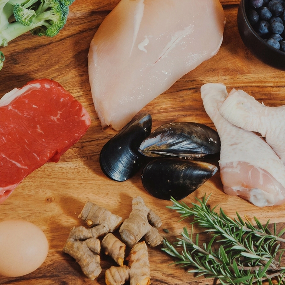 Raw fresh meat, veg and garnishes on wooden cutting board.