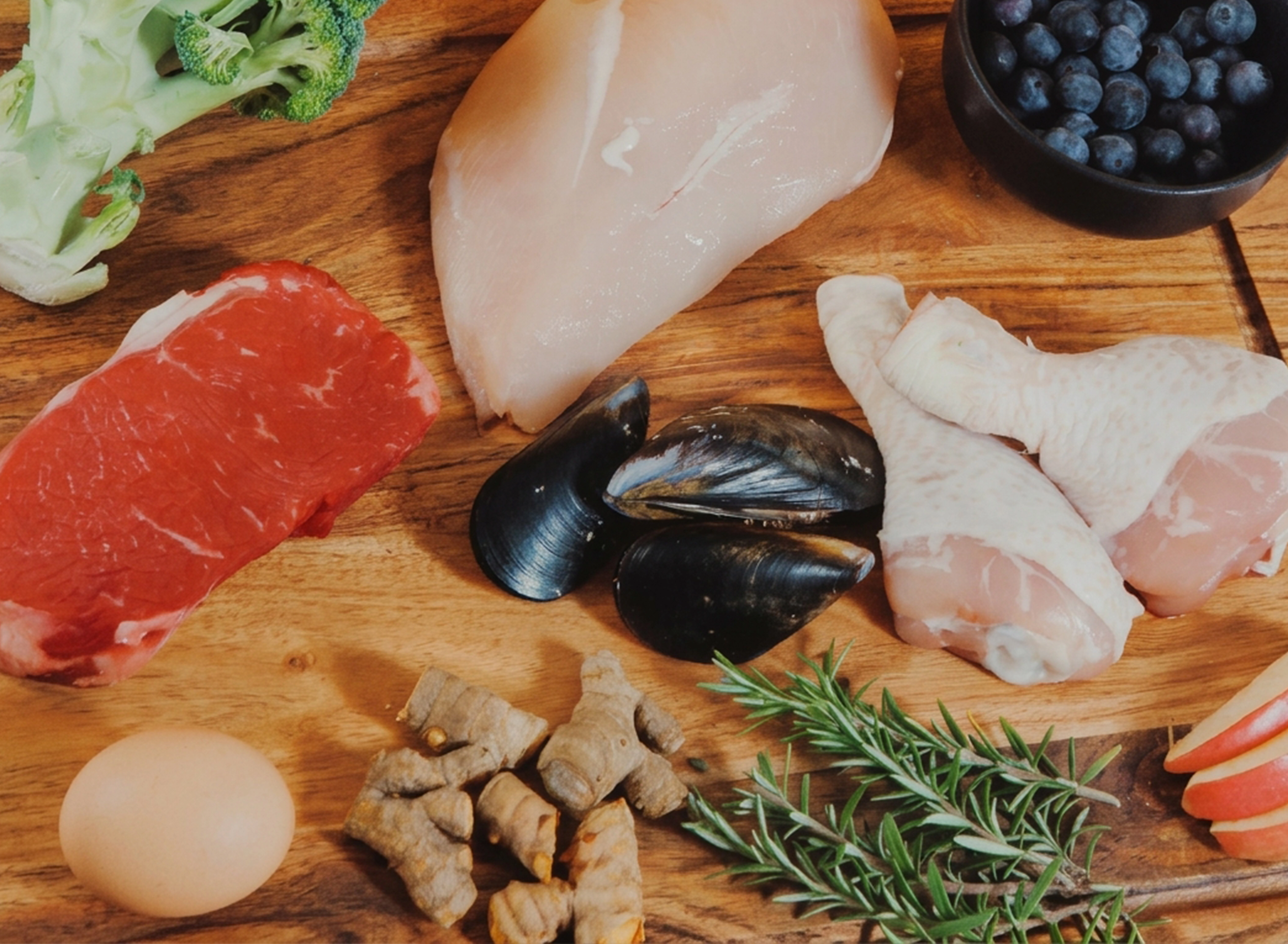 A variety of raw foods including meat, seafood, fruits, and vegetables are displayed on a wooden board.