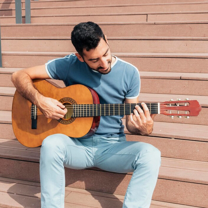 Man sitting on steps playing an acoustic guitar.