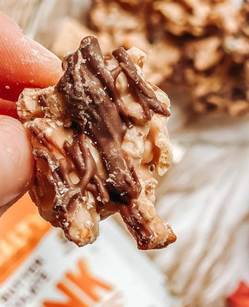 Close-up of a hand holding a chocolate-drizzled snack cluster.