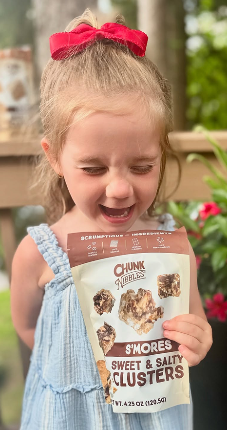 Child holding a bag of s'mores sweet and salty clusters, smiling outdoors.