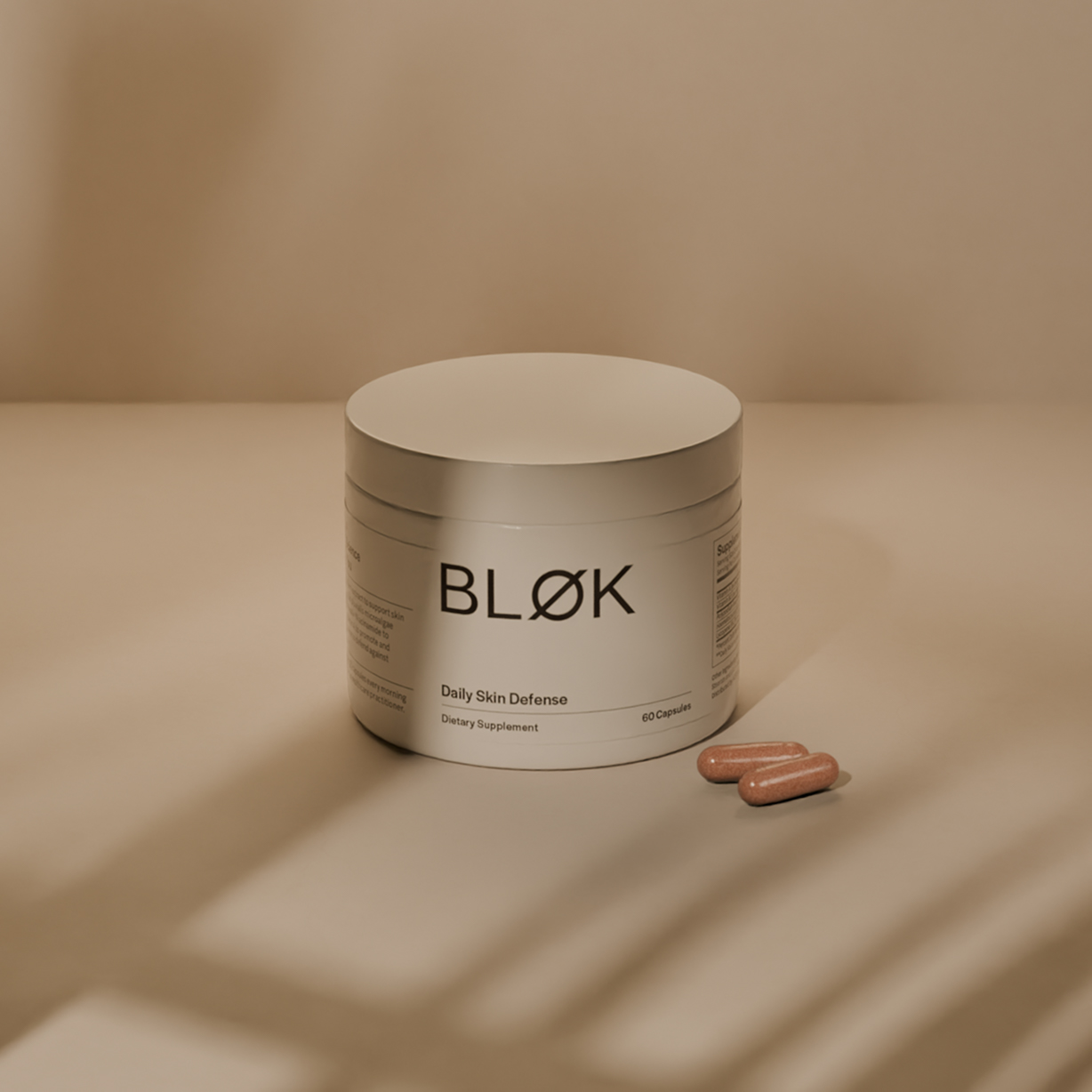 A jar labeled 'BLØK Daily Skin Defense' with two capsules beside it.