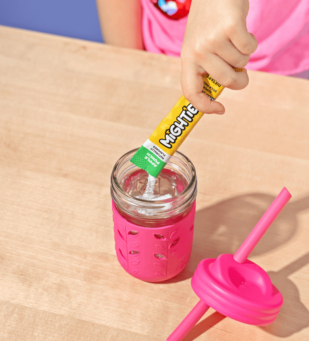 Hand pouring powder from packet into a jar with pink sleeve and lid.
