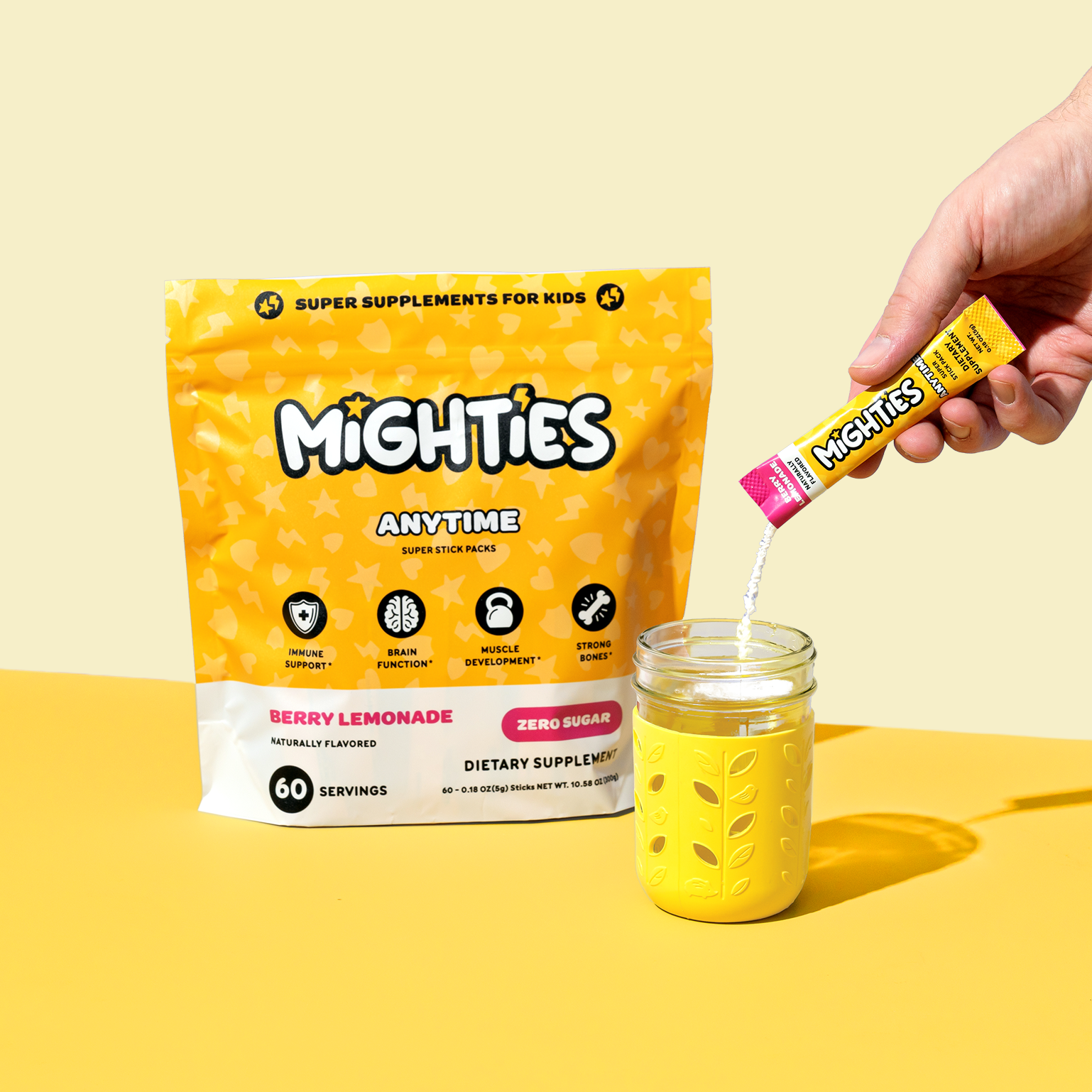 Hand pouring Mighties supplement into a glass, with product packaging in the background.